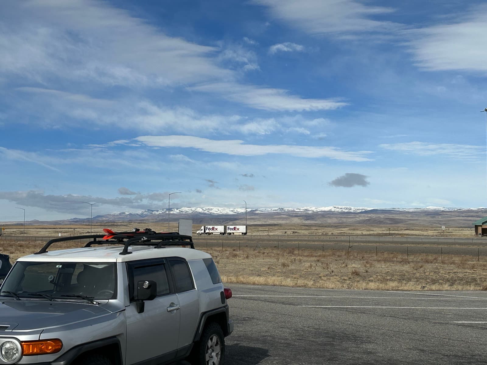 Silver Toyota FJ Cruiser with skis on the roof rack, snowy mountains in the distance